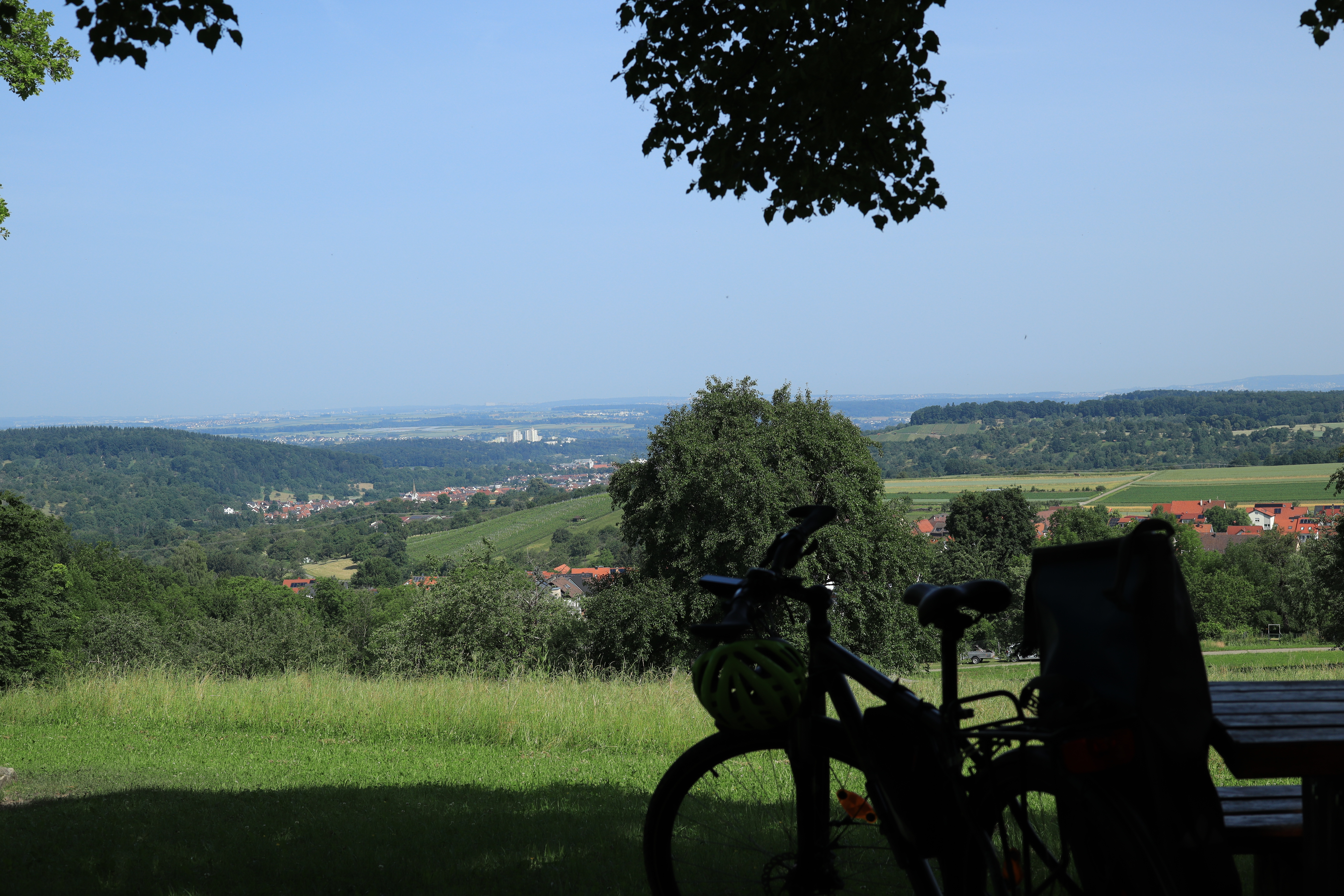 A blurry dark bicycle in the foreground and a sunny landscape behind it.