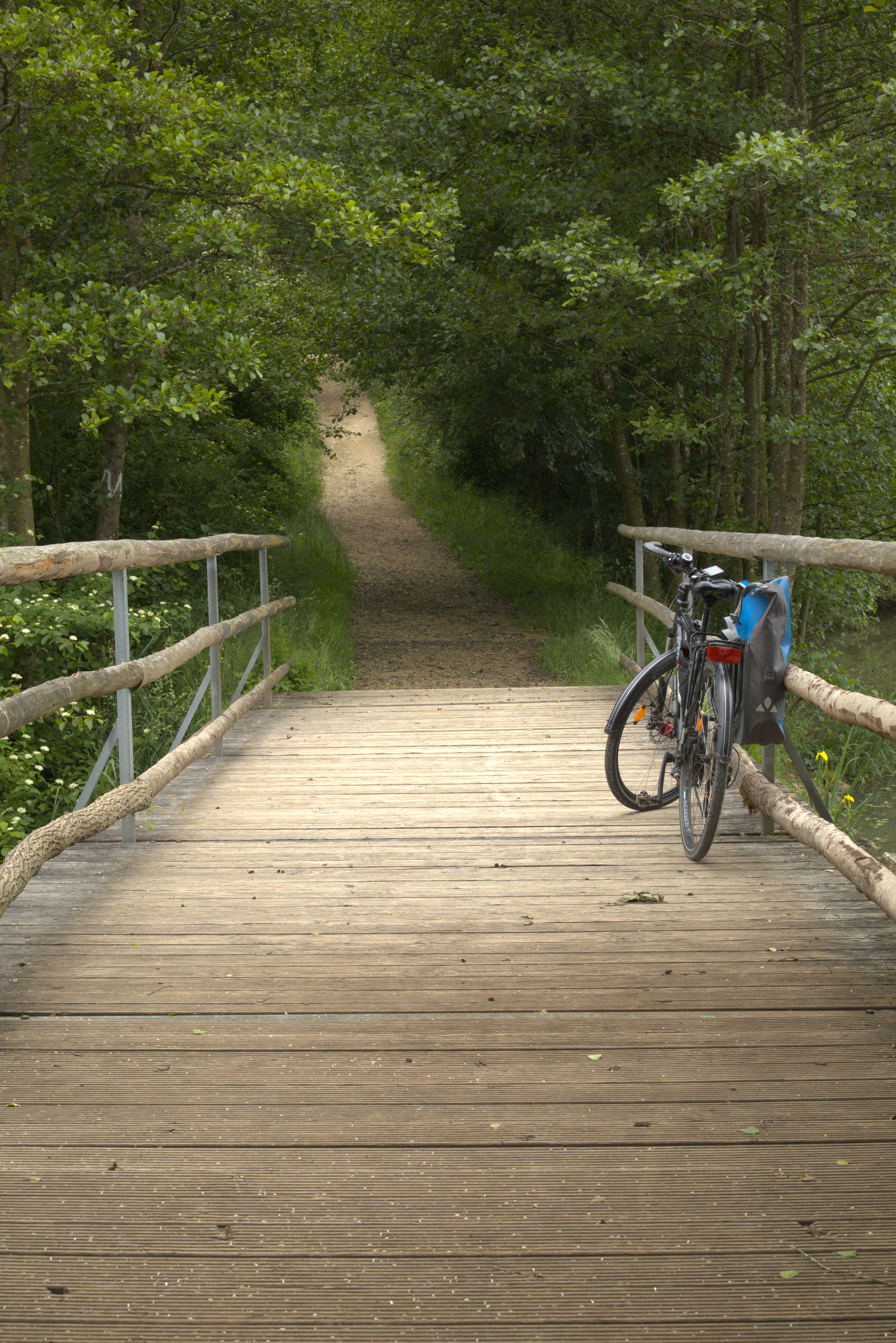 A black bicycle on the side of a bridge-looking wooden structure, which is a top of a dam. A gravel trail continues past the dam.